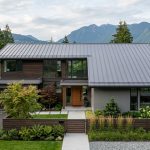 A contemporary Vancouver home featuring a newly installed standing seam metal roof with charcoal gray panels, neat landscaping, and North Shore mountains in the background.