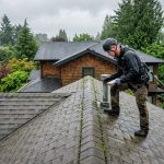 Licensed roofing contractor inspecting a residential roof in Vancouver on a rainy day, checking shingles for damage with moss visible, conveying expertise and local knowledge.